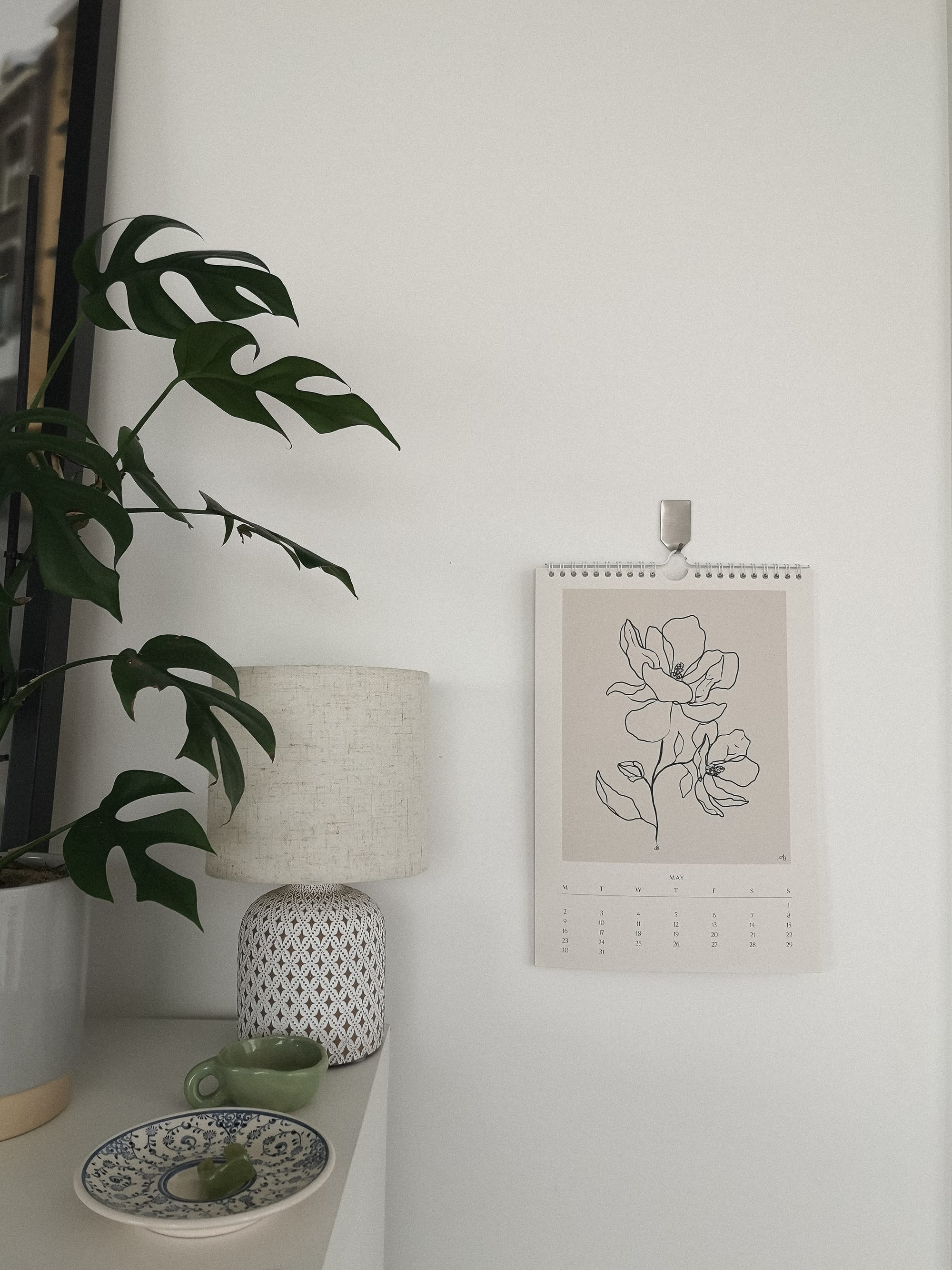 painting of a white flower near white lamp and a green plant.