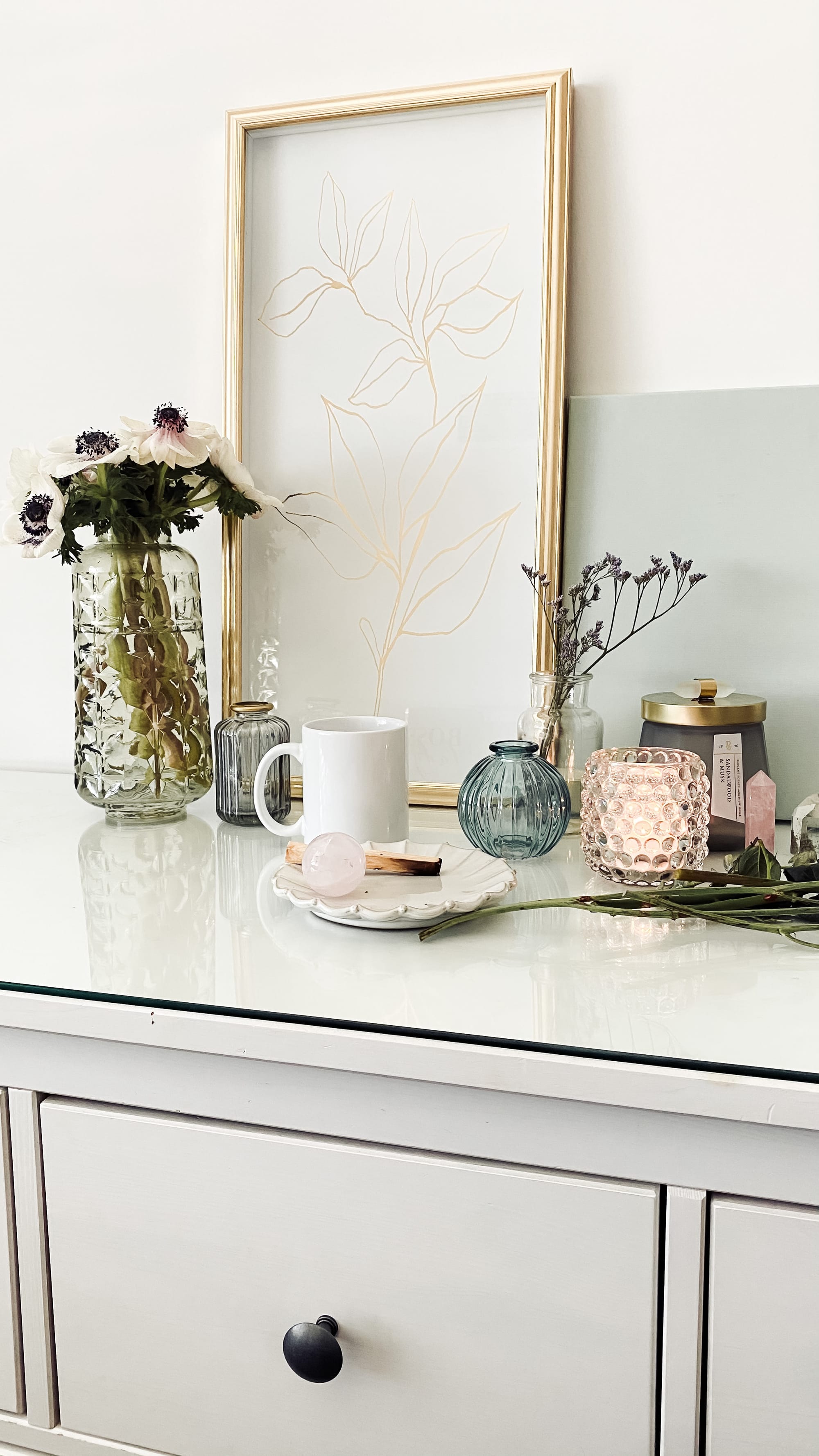 White drawers with ceramic bowls, candles, art and flowers.