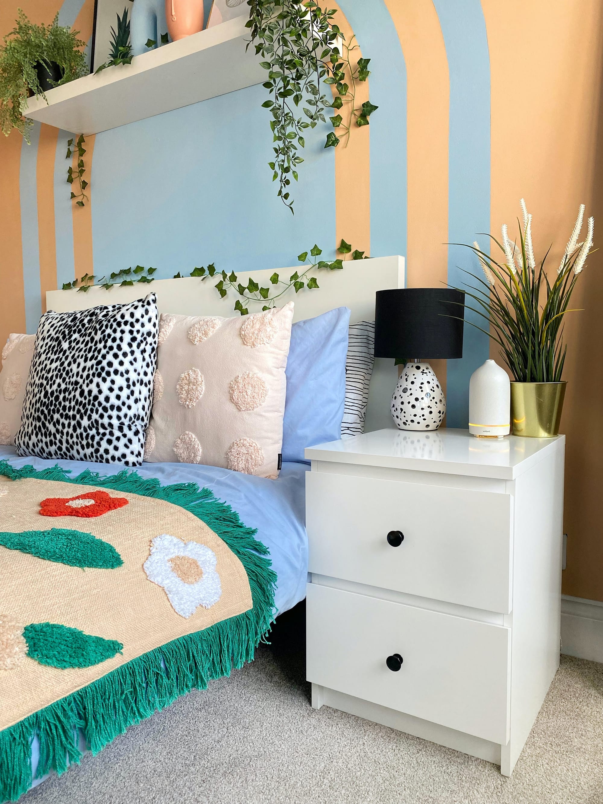 A colorful blue and green bed with a orange and blue accent wall with patterned throw pillows